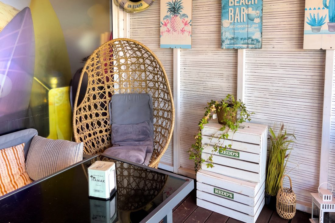 Die Beach Bar Hamak Podczele in Kolberg mit Korbstuhl, Sofa sowie Rettungsring und Bildern wie von Surfbrettern an den Wänden.