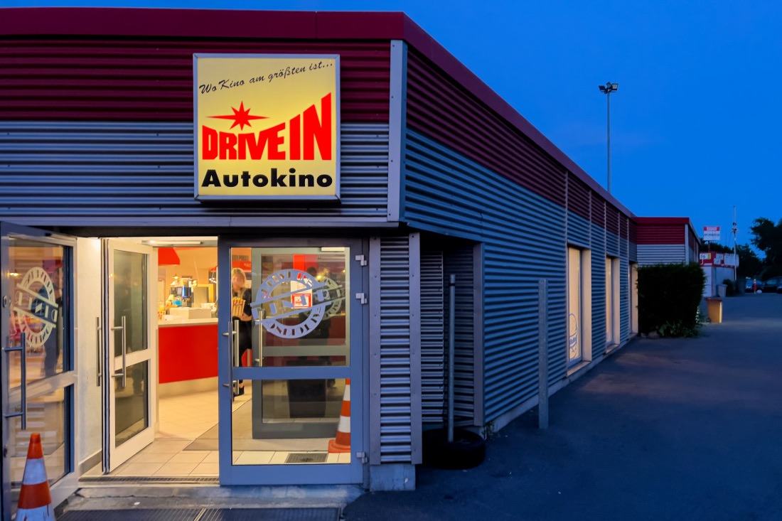 Eingang zur Snackbar vom Autokino Essen. Oben an dem kastenförmigen Gebäude hängt ein Leuchtschild mit "Drive in Autokino".